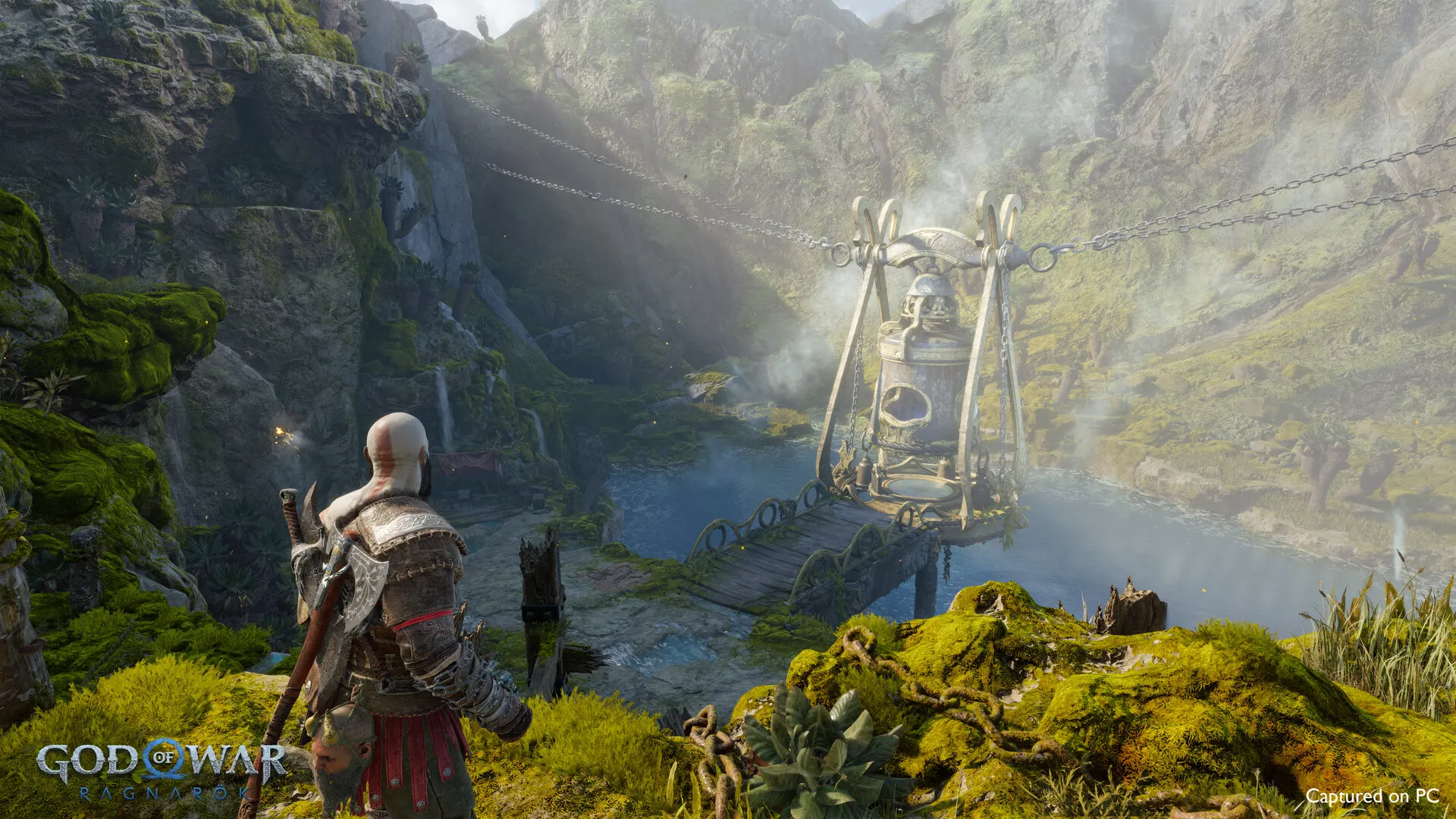 Kratos, vu de dos sur une falaise couverte de mousse, domine un défilé brumeux où pend une cage suspendue